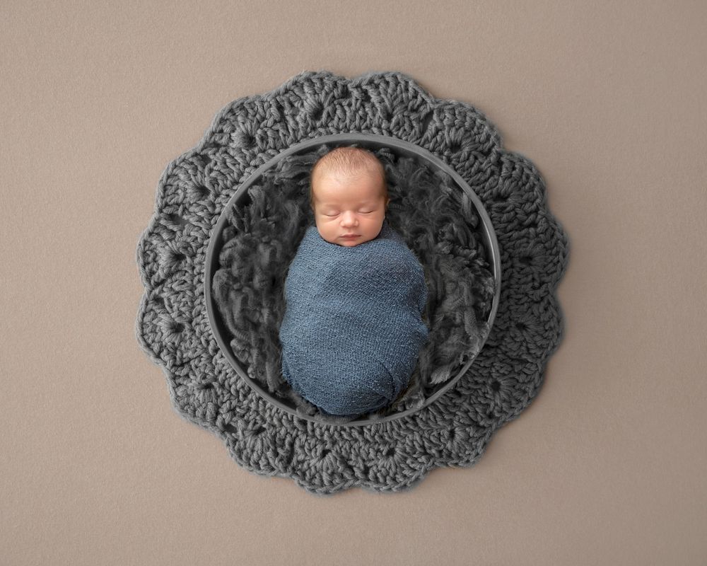 Newborn Boy snuggled up cosy in a blue wrap placed on a digital backdrop. In home Newborn session with Bump Birth and beyond