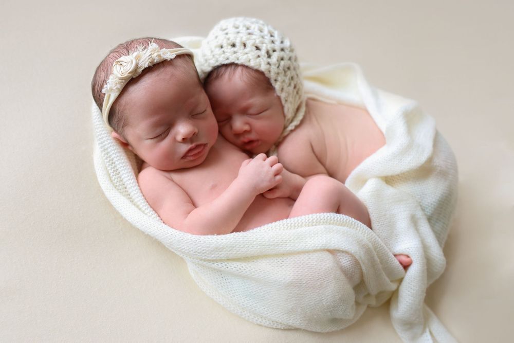 Twin newborn session, two newborn twins photo on a cream backdrop and cream wrap.