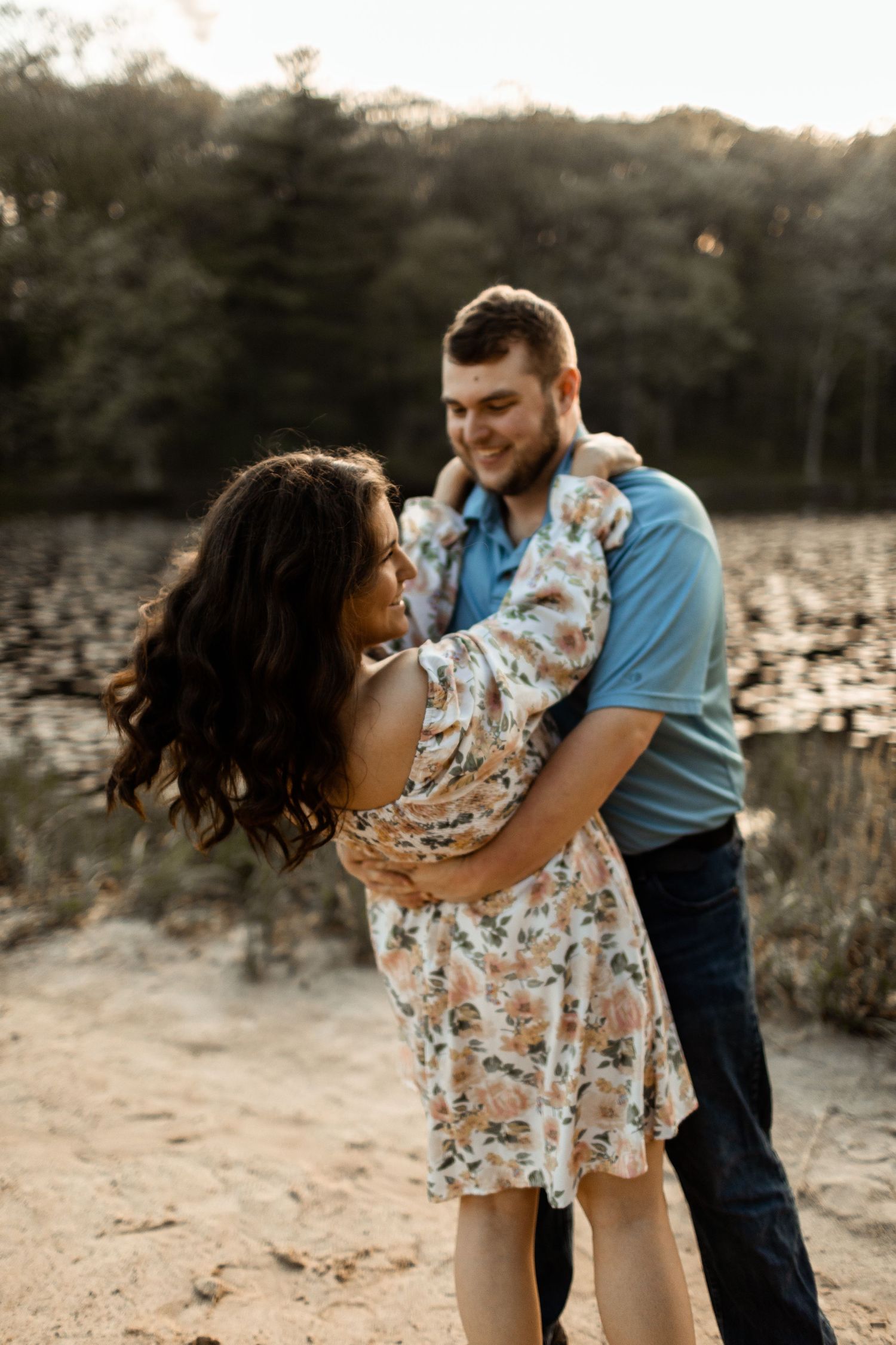Couple sharing romantic moment by lake at sunset in casual outdoor setting.