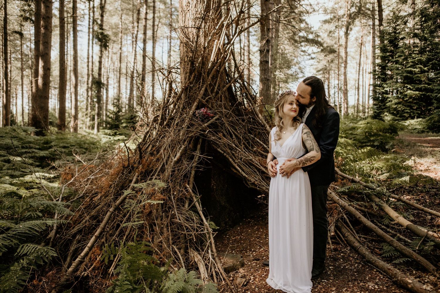 bride and groom in the forest in front of man made branch house