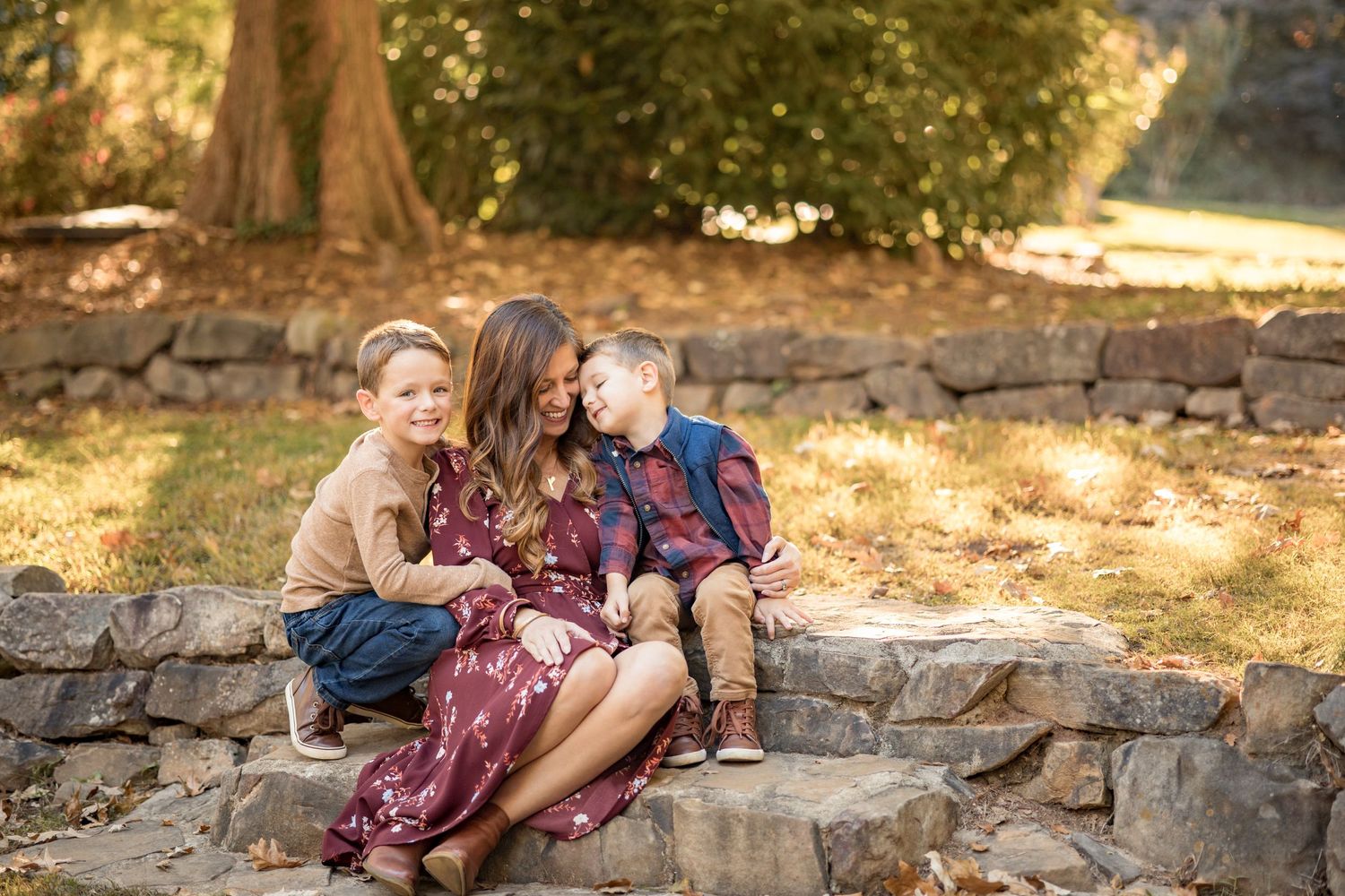 Family sitting together on rustic stone steps surrounded by autumn foliage in outdoor portrait session.