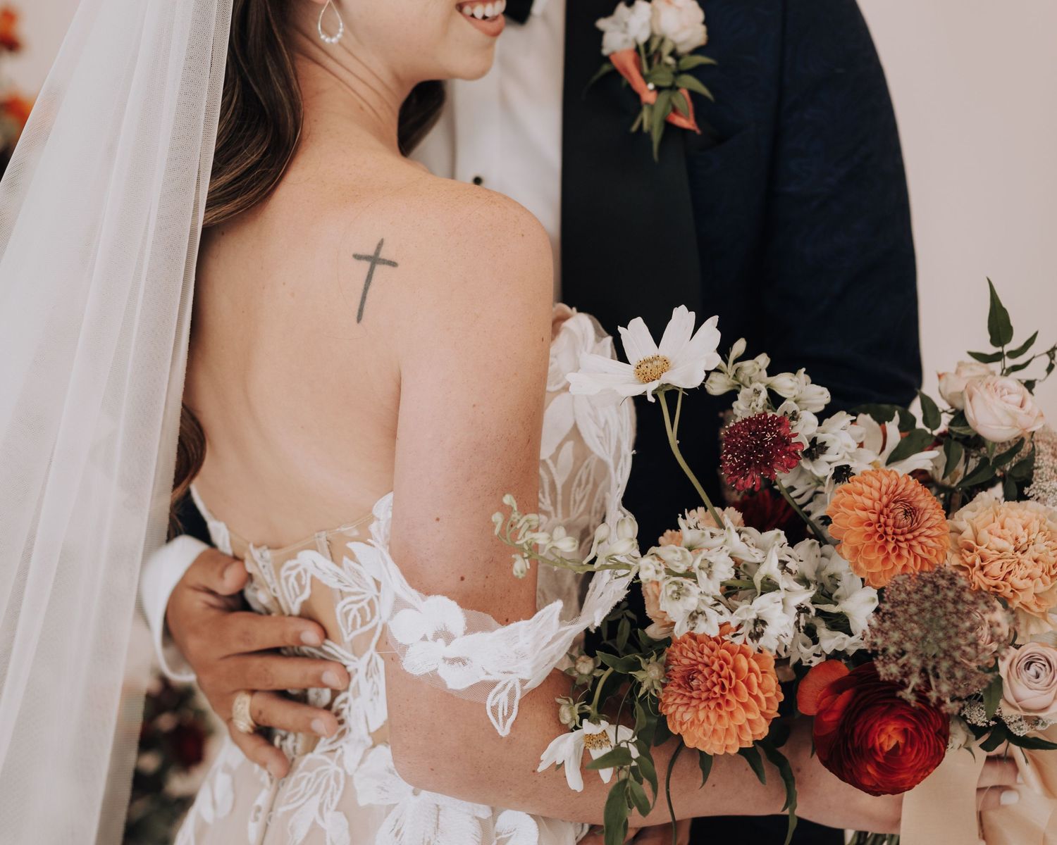 Close-up of lace wedding dress detail and cross tattoo with autumn-colored bouquet.