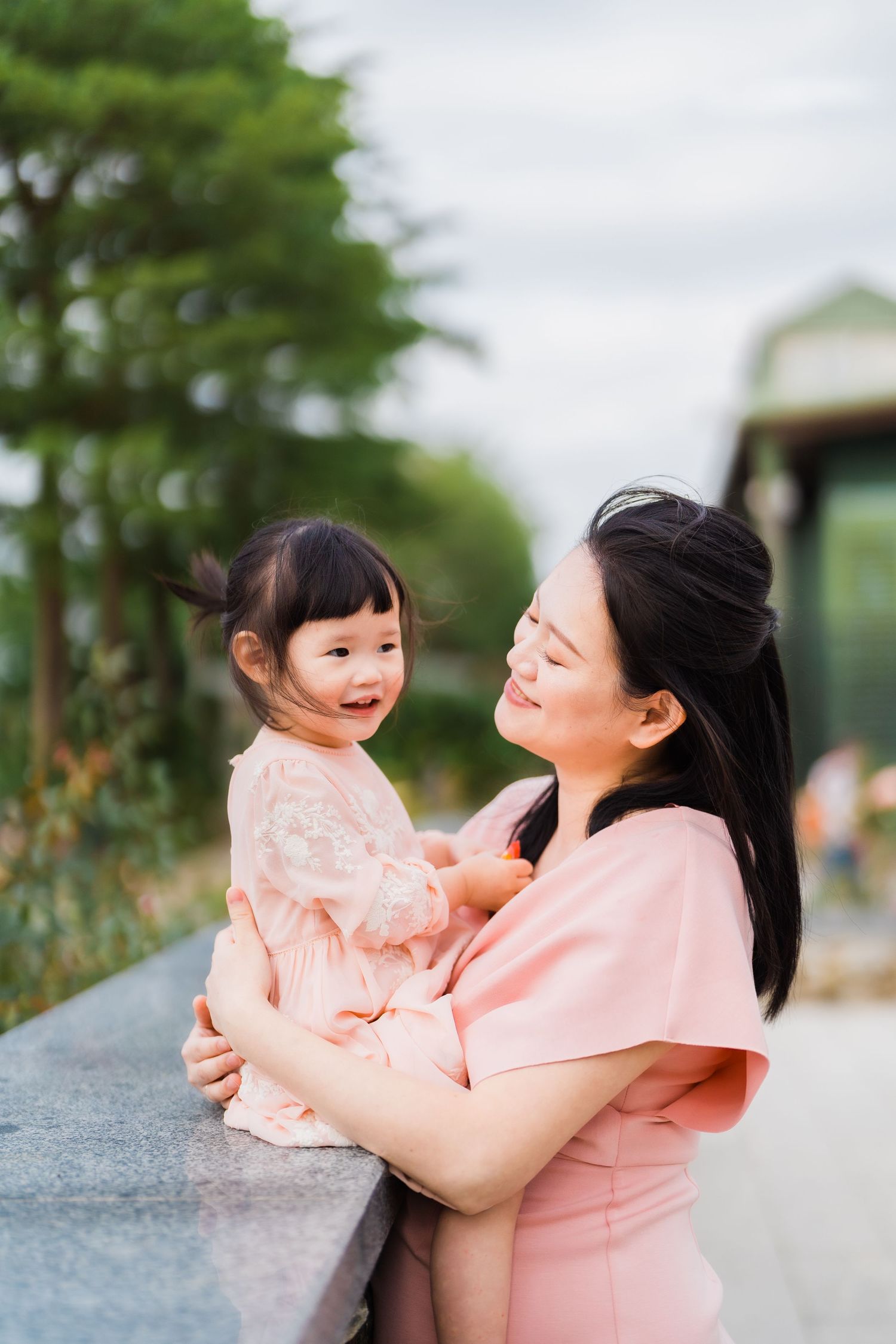 Mother and daughter wearing matching pink outfits embrace during an outdoor photoshoot.