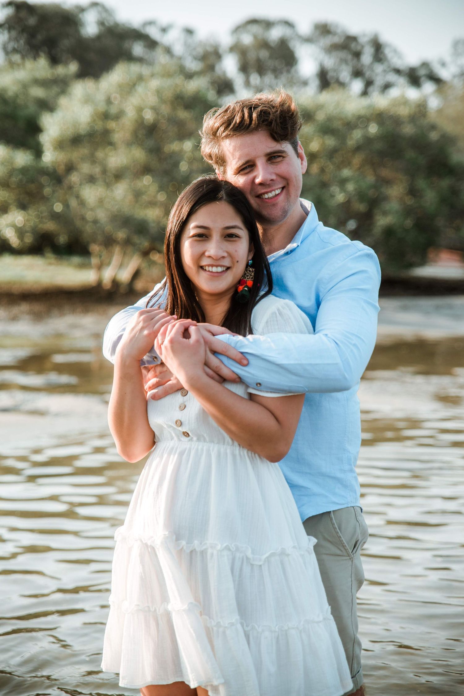 A happy couple embraces while standing in shallow water with trees in the background.