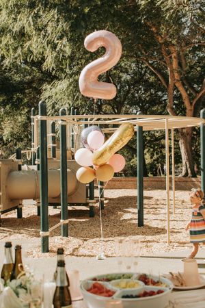 Outdoor party setup with pink and gold balloons hanging from wooden beams.