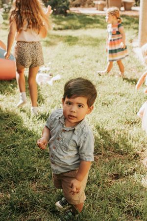 Child playing on grass during an outdoor party with festive decorations in background.