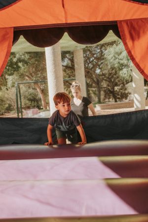 Child playing in an orange and black bounce house with outdoor pillars visible in background.