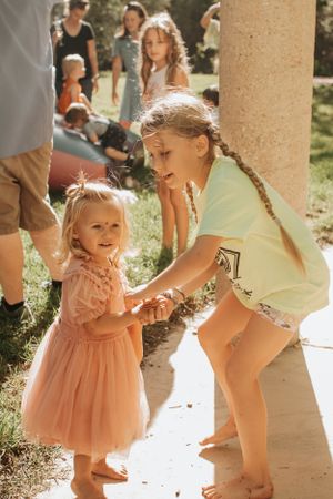 Two people in summer outfits interacting at an outdoor gathering near stone pillars.