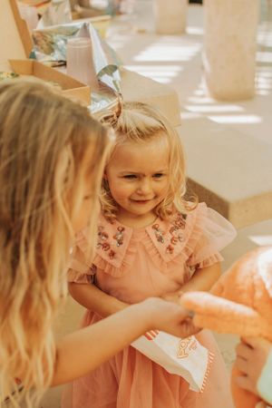 Children at a party sharing treats and smiling in warm sunlit setting.