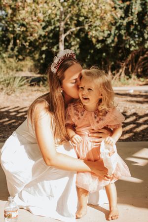Sweet moment captured in outdoor sunlit setting with pink dress and white outfit.