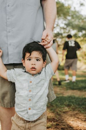 Small child in grey shirt holding adult's hand while standing outdoors.
