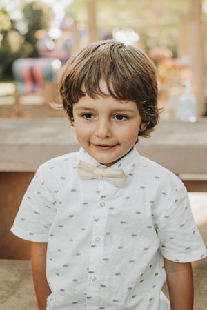 A young child wearing a white shirt and bow tie smiles at the camera.
