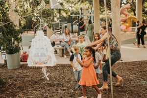 Children playing and jumping around a suspended white decoration in an outdoor garden setting.