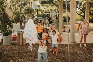 Children playing and reaching up toward hanging white decorations in a garden space.