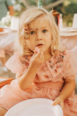 A small child in a pink dress eating at an outdoor party.