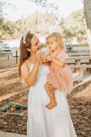 Two people in white dresses share a tender outdoor moment in warm sunlight.