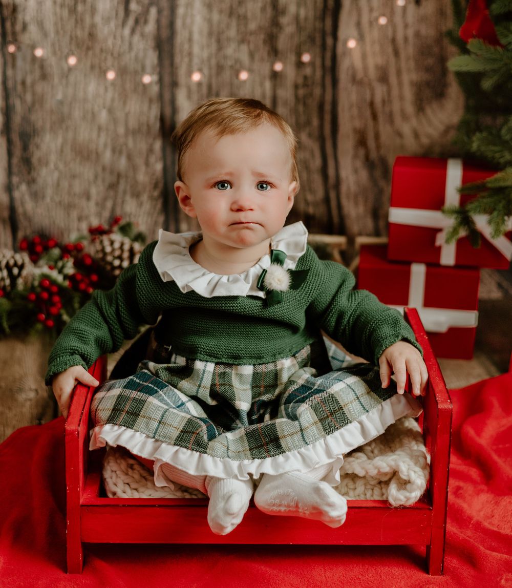 baby girl in green dress on a red bed at christmas