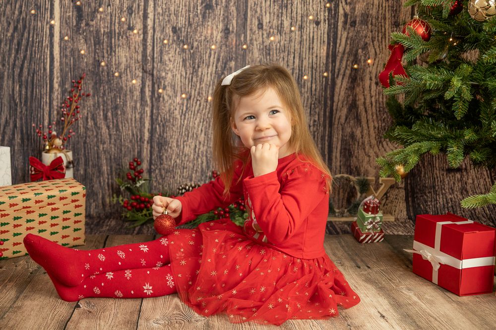 little girl in red Christmas dress with hand under chin