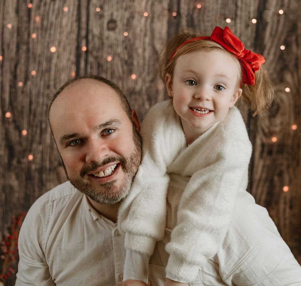 father and daughter christmas photo in white with lights at the back