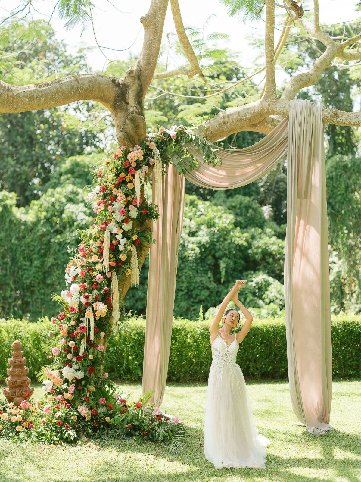 Elegant outdoor wedding arch decorated with flowing blush fabric and floral arrangements in a garden setting.
