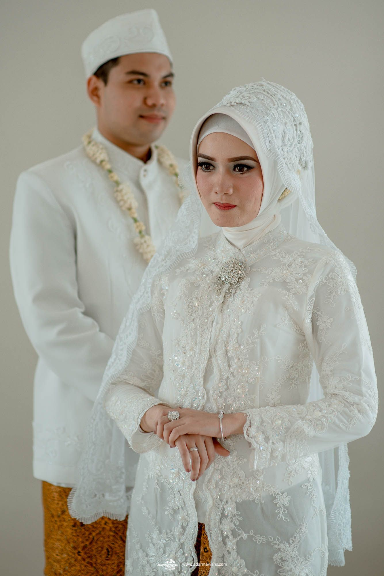Elegant Indonesian wedding couple in traditional white and gold ceremonial attire.