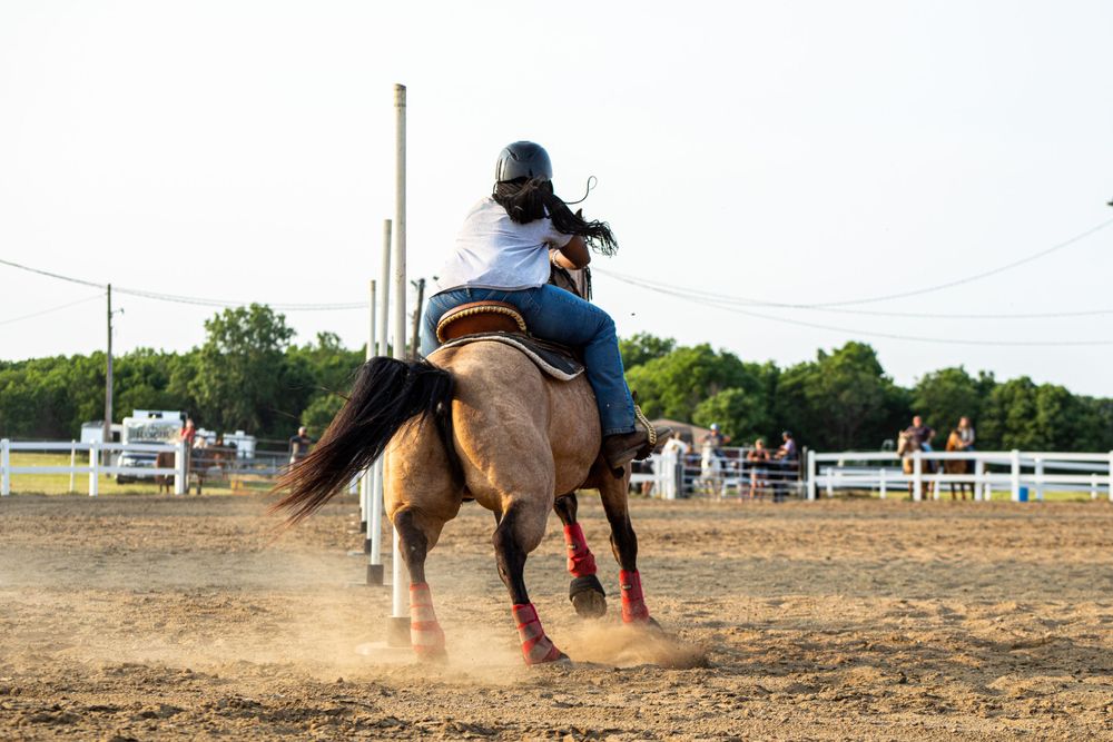 Horse and rider practicing barrel racing patterns in outdoor arena.