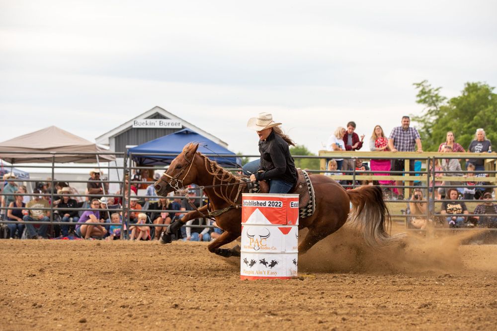 Barrel racing competition with horses and riders navigating turns in dusty arena.