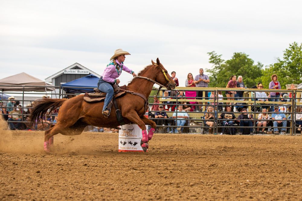Barrel racing horse leaning into turn at high speed during rodeo event.