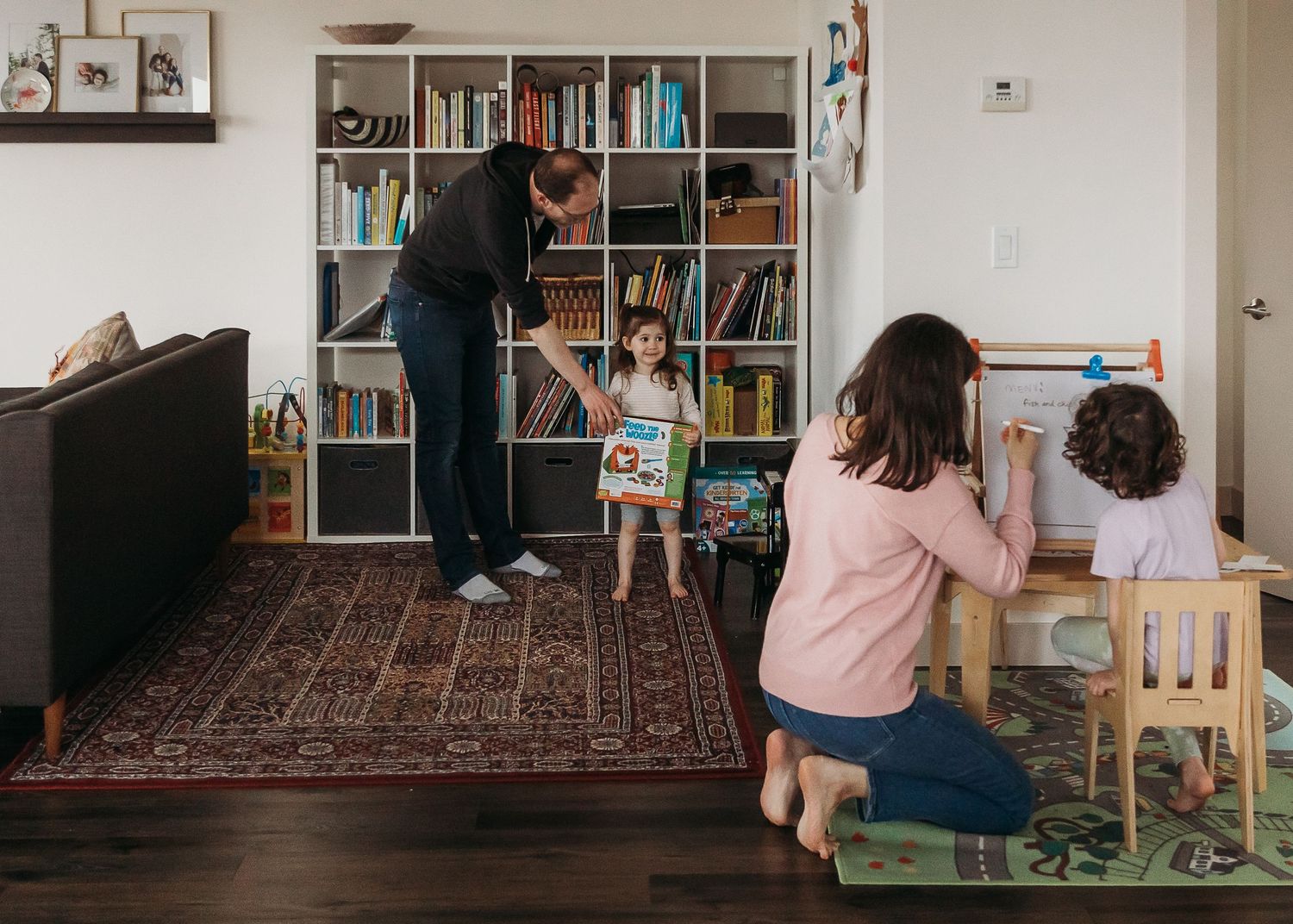 Family engaged in measuring height against bookshelf wall in living room.