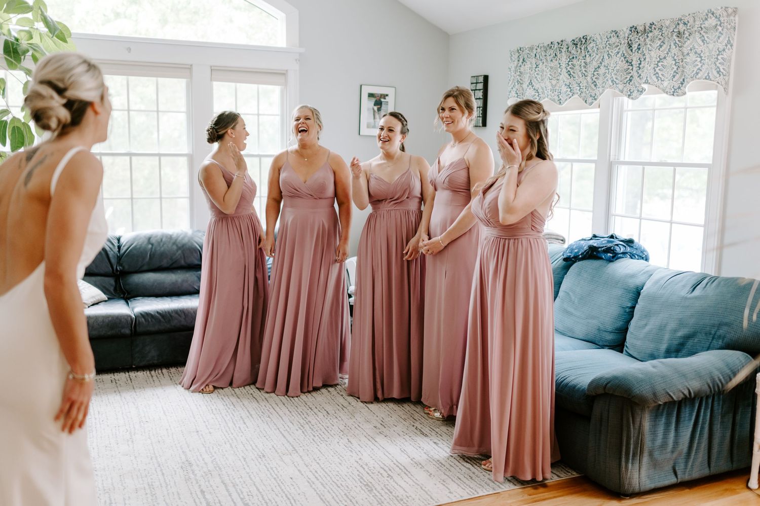 A group in dusty rose dresses gather in a bright room with white walls and modern furniture.