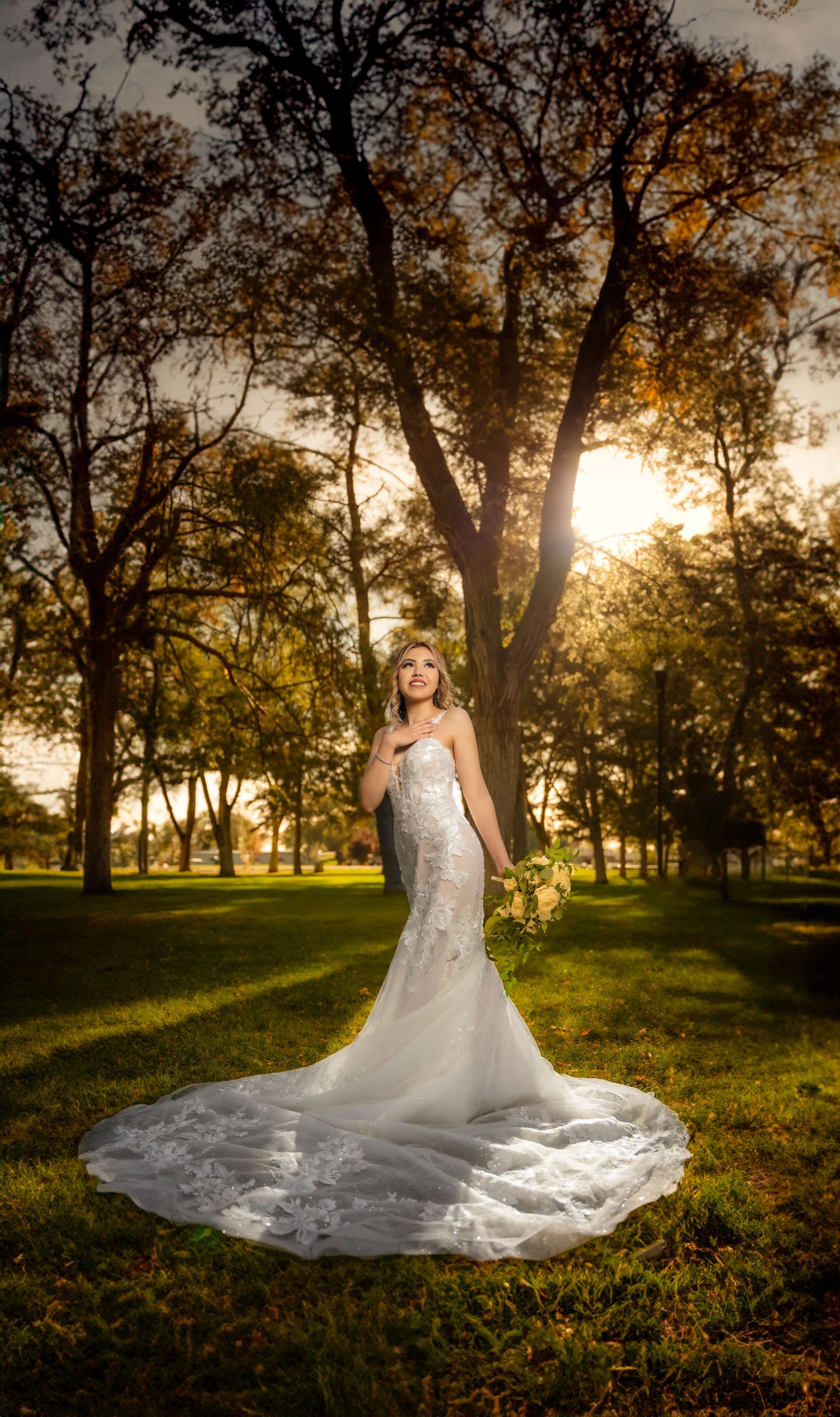 Bride in a white lace mermaid wedding gown holding a bouquet in a sunlit autumn park.
