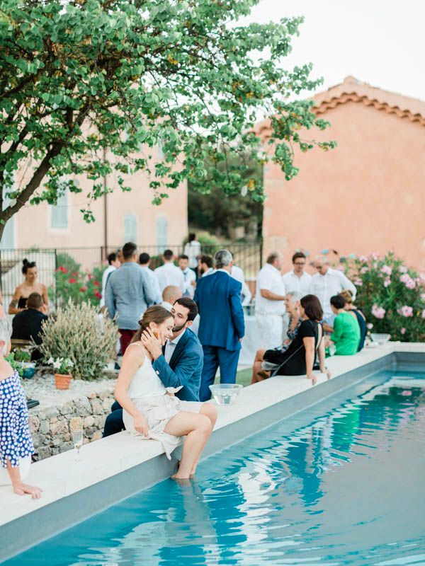 Les invités se rassemblent autour d’une piscine lors d’un élégant événement en plein air, avec une architecture méditerranéenne