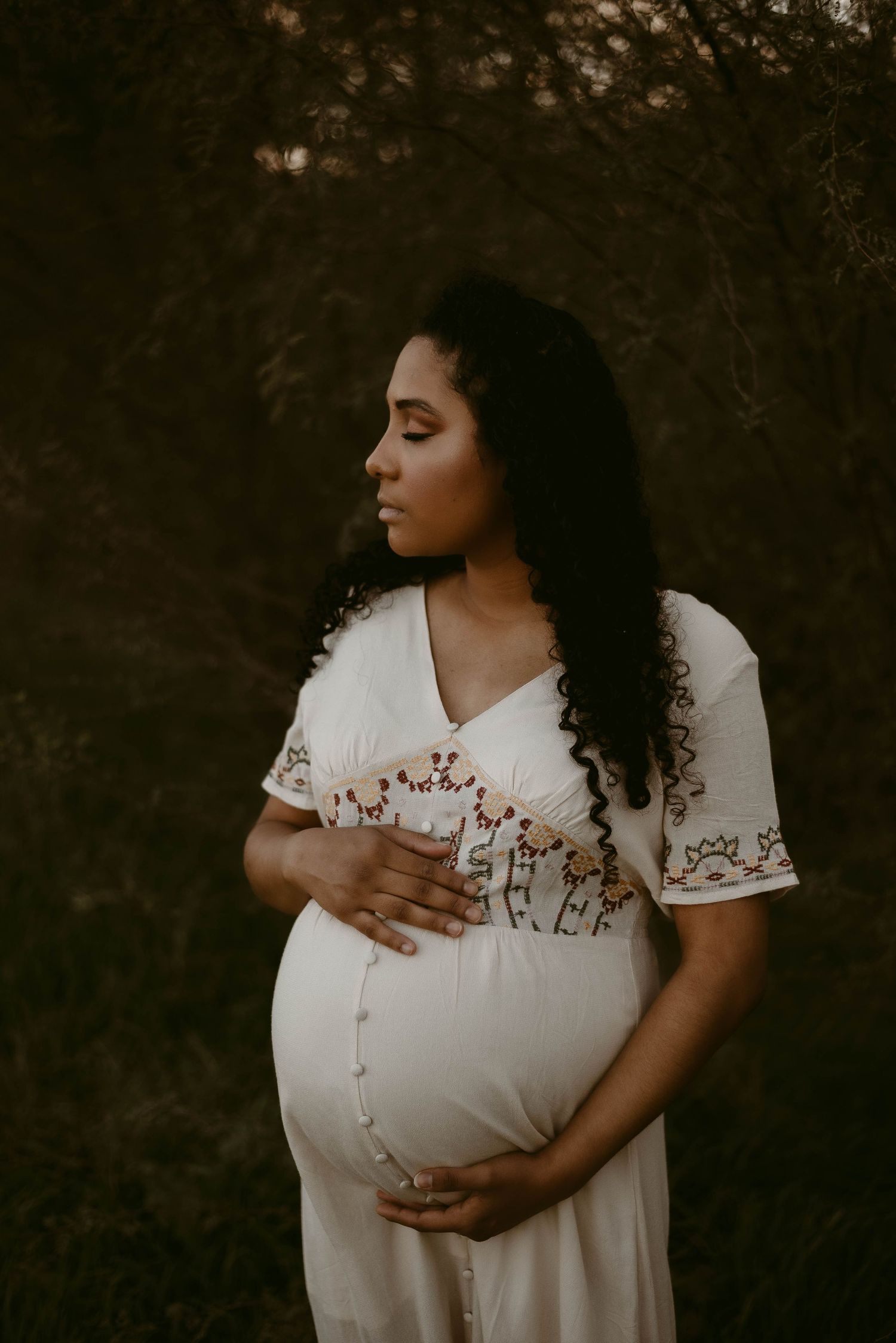 Intimate maternity portrait in an embroidered white dress captured during golden hour.
