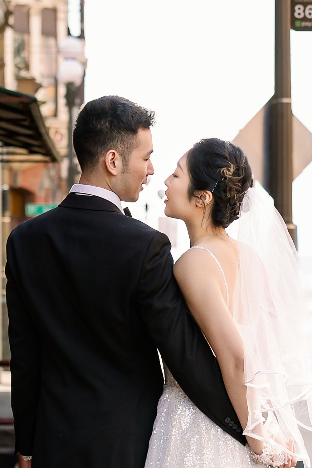 Bride and groom share an intimate moment gazing at each other on a sunlit city street.