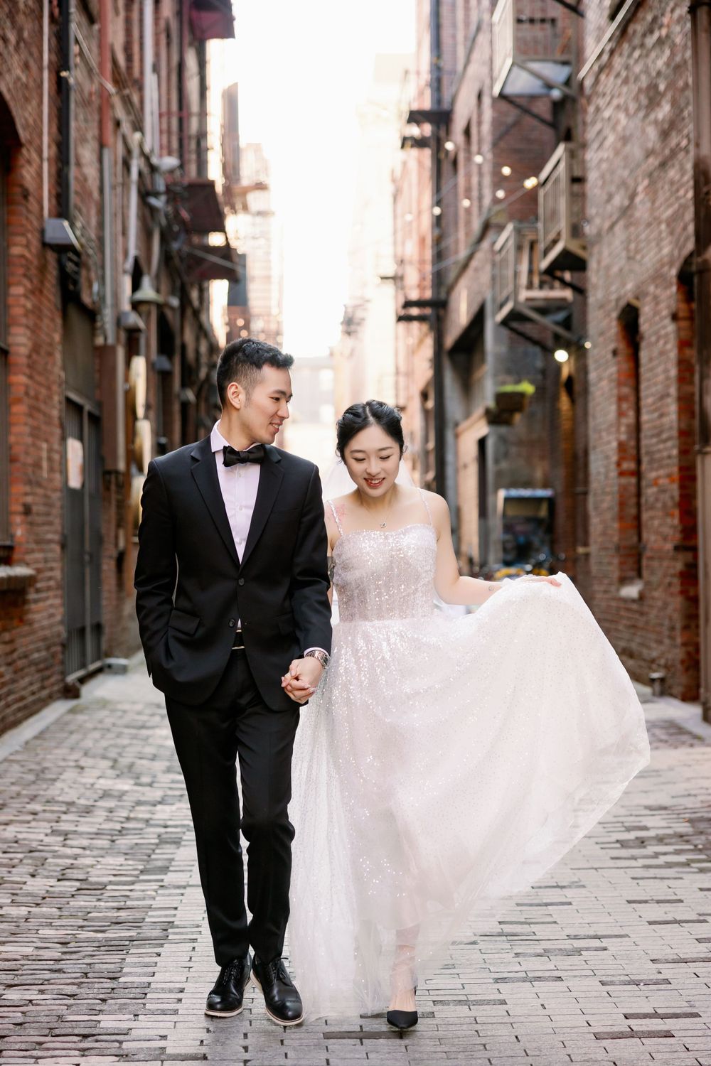 Bride and groom walk hand in hand through charming brick cobblestone alley in Seattle.