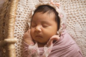 Sleeping newborn in pink lace bonnet resting on cream crochet blanket.