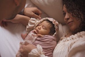 Peaceful newborn baby wearing pink clothing and lace bonnet sleeping soundly.