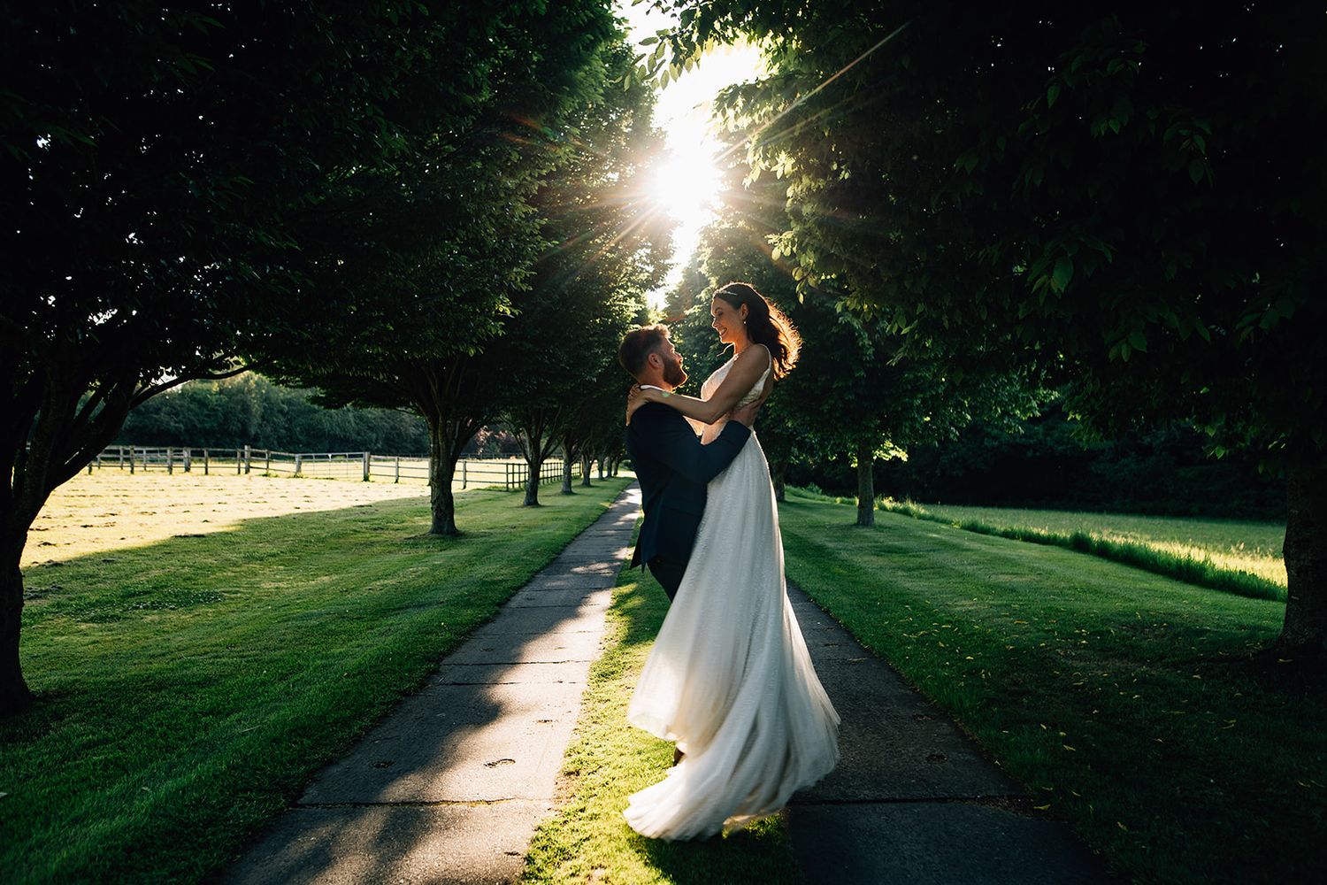 A wedding couple walking in a park at sunset with dramatic backlighting creating silhouettes.