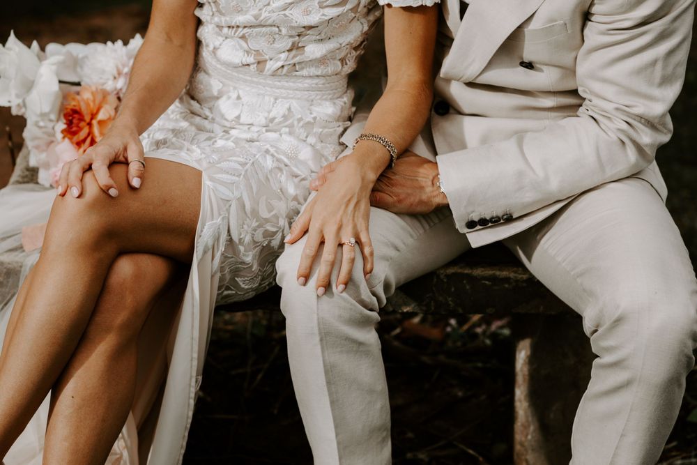Close-up detail of couple's hands resting together on white and beige wedding attire.