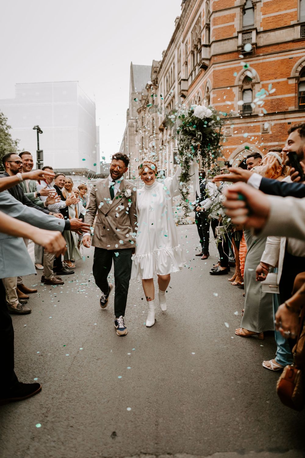 Wedding guests throw confetti as newlyweds walk through a celebratory exit line.
