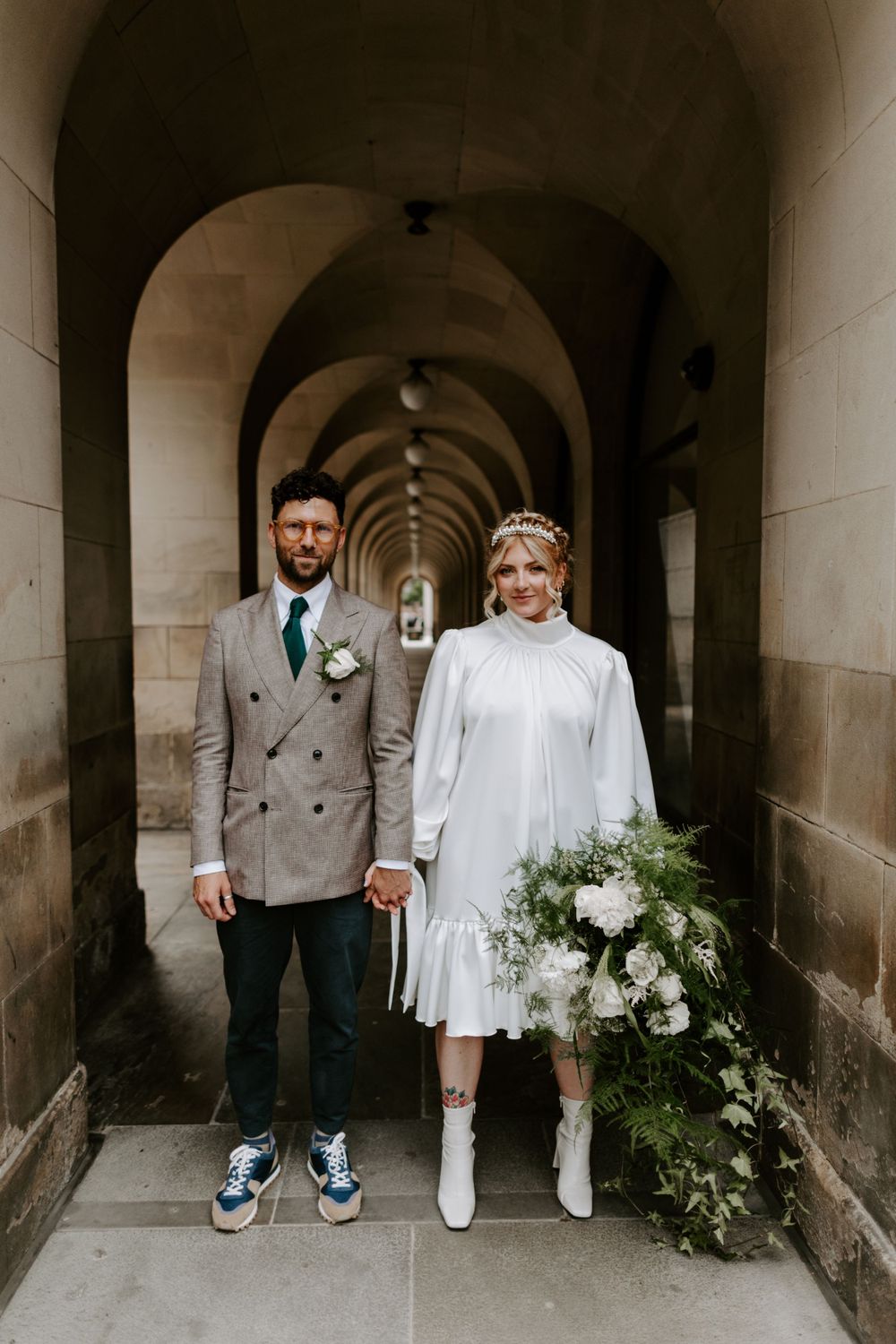 A modern couple poses in a columned archway wearing contrasting formal attire.