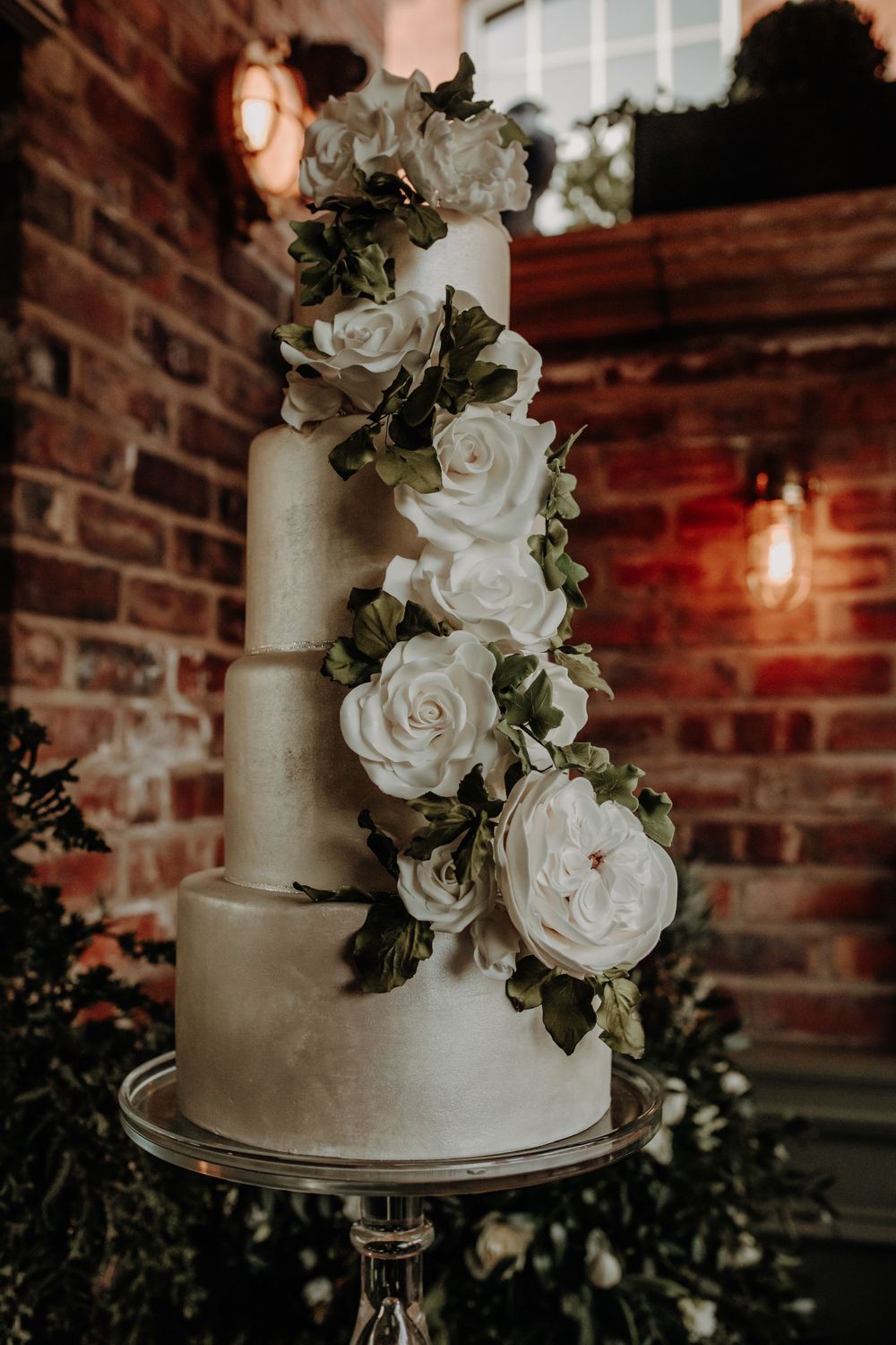 An elegant white wedding cake decorated with cascading sugar roses against a brick wall background.
