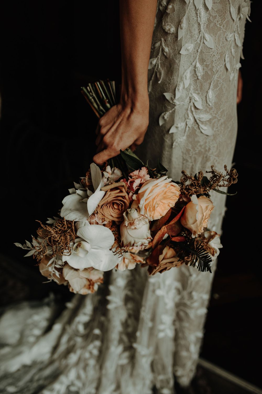 A bridal bouquet with peach and white roses against a textured wedding dress.