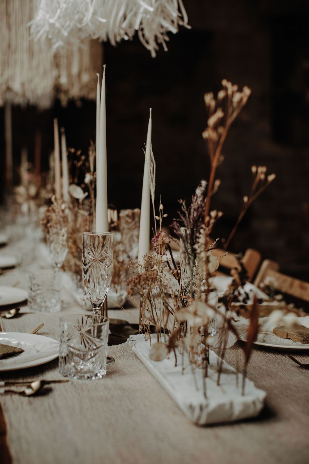 Moody wedding table setting with tall white candles and dried flower arrangements.