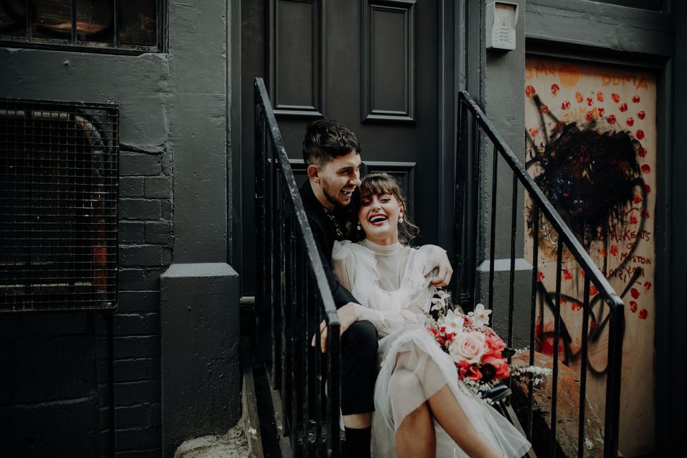A romantic couple shares a moment on black stairs with floral bouquet.