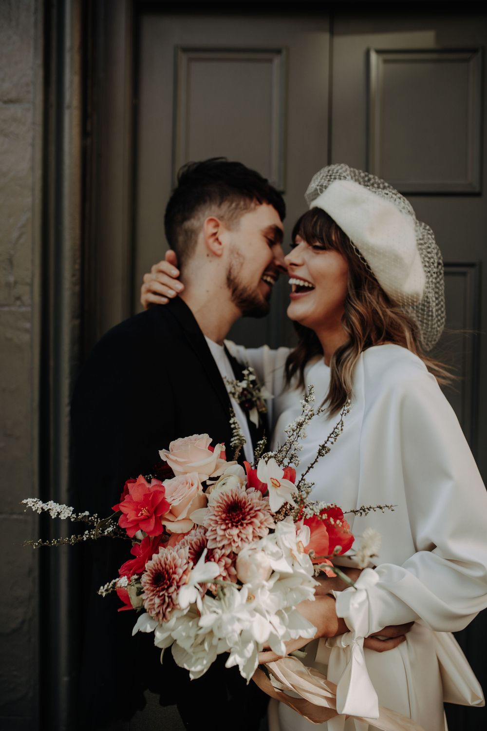 A romantic couple shares an intimate moment while holding a vibrant bouquet of pink and white flowers.