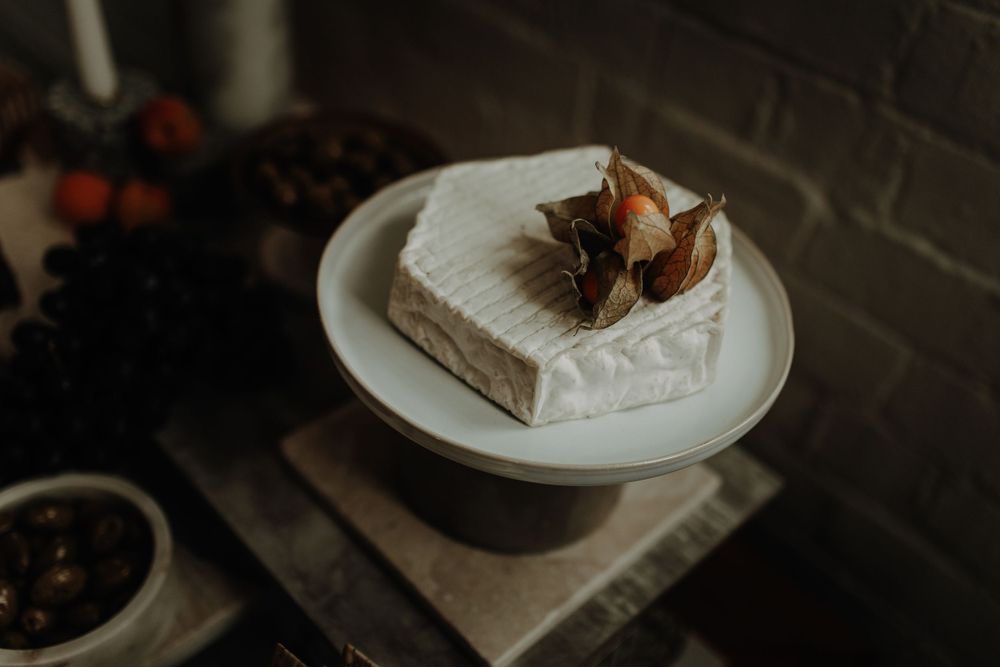 A rustic white cake topped with dried flowers sits on a ceramic cake stand.