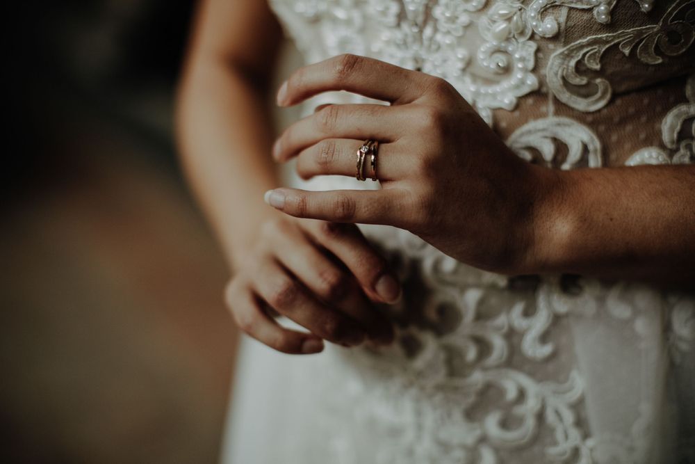 Close-up detail of hands with wedding ring against intricate lace dress pattern.