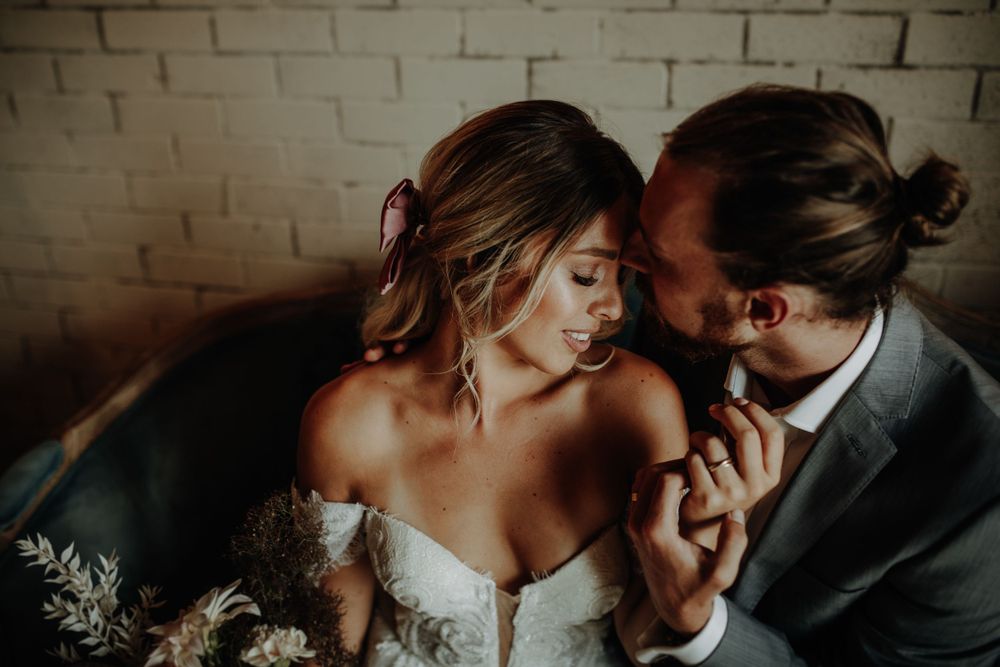 Intimate wedding moment captured in moody lighting against white brick wall.