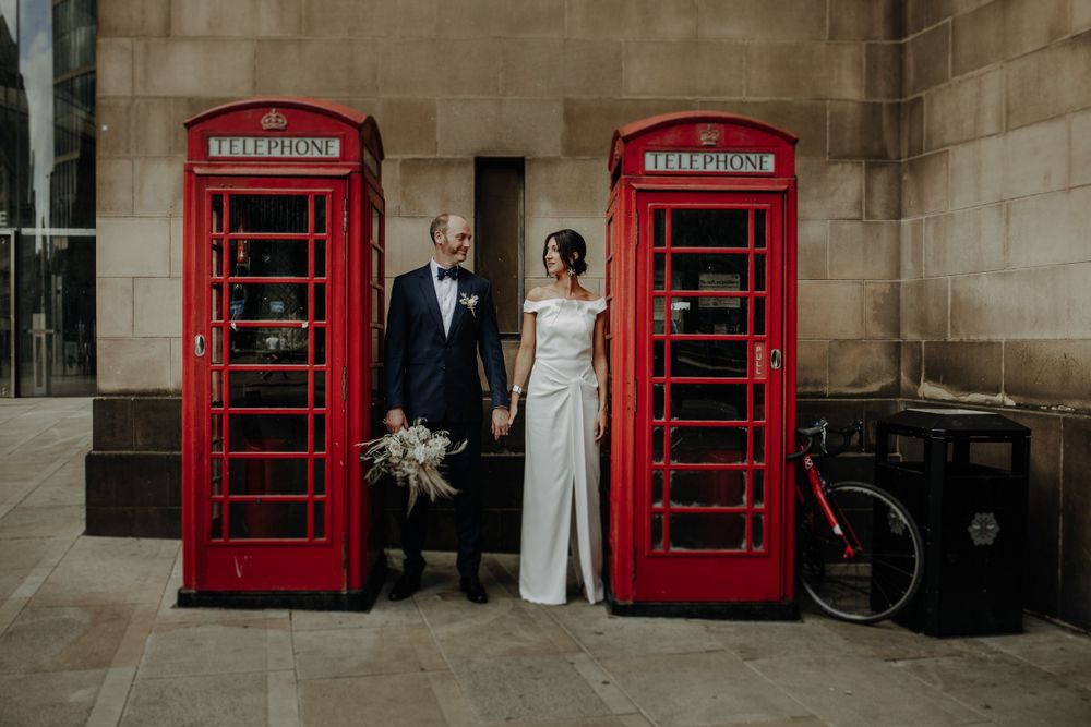 Wedding couple poses between iconic red British phone booths in formal attire.